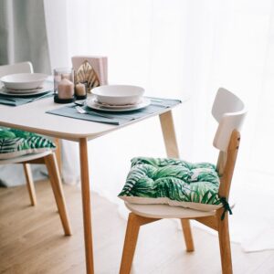 Contemporary dining room with wooden furniture and green-leaf cushions. Bright and inviting.